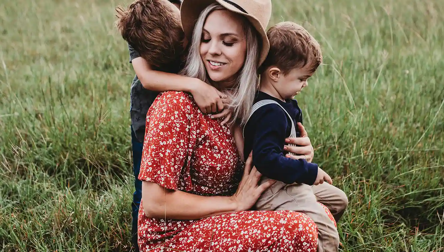 Mother enjoying time with her two young sons, embraced by one and hugging the toddler