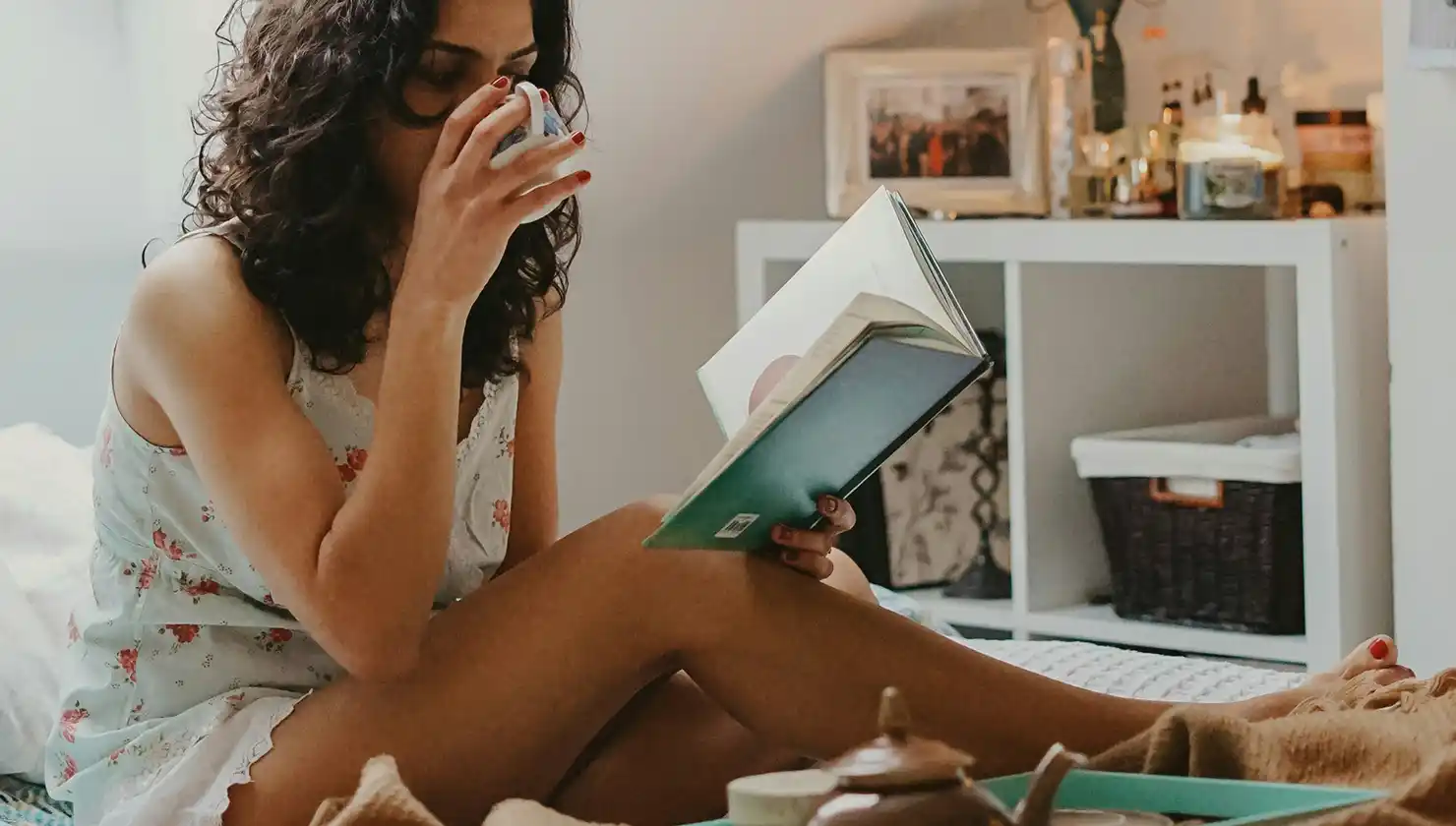 Potential breast augmentation patient in recovery resting in bed with tea and a book
