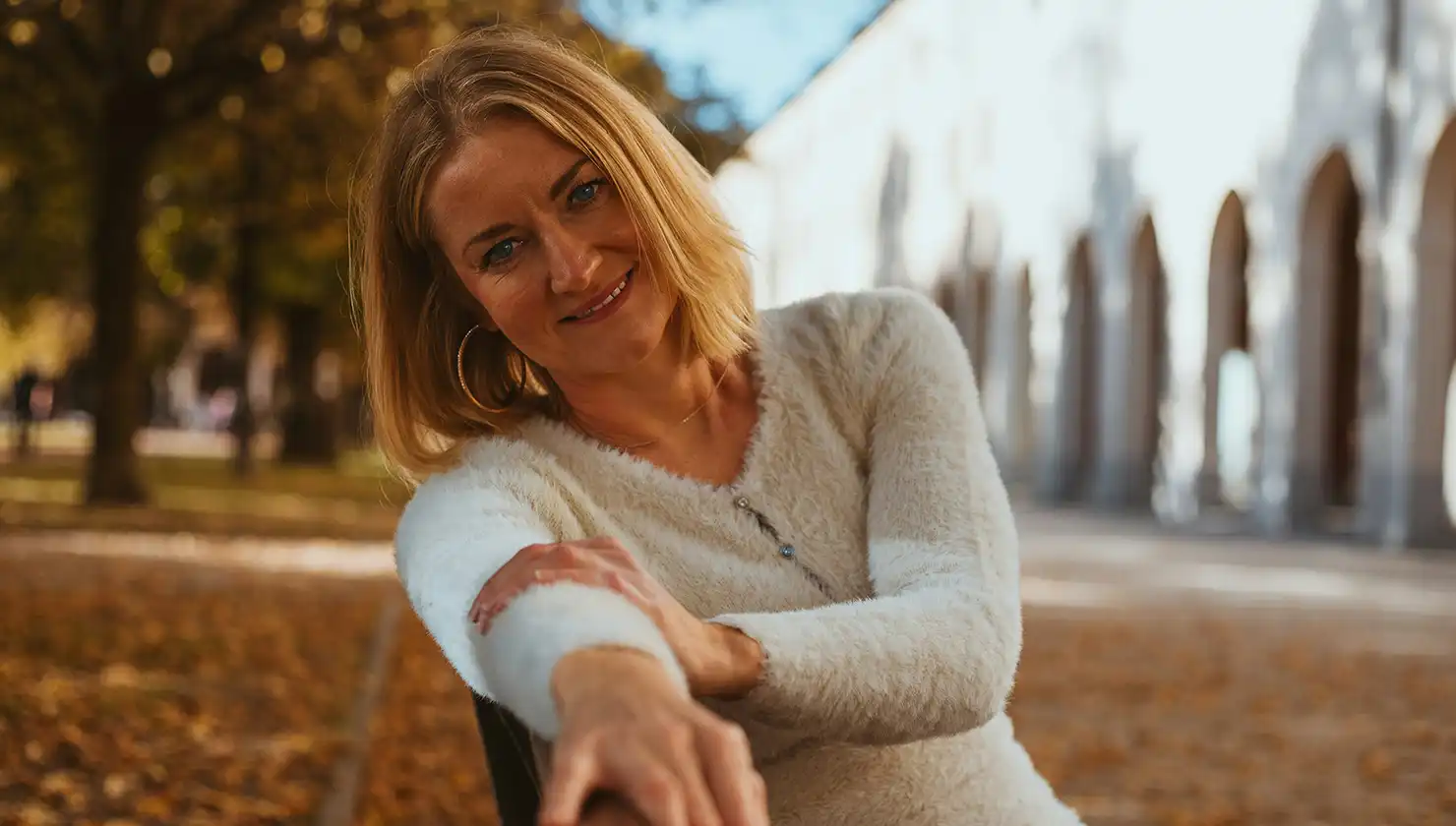 woman sitting on a bench outside smiling - potential patient for blepharoplasty and fillers or fat grafting